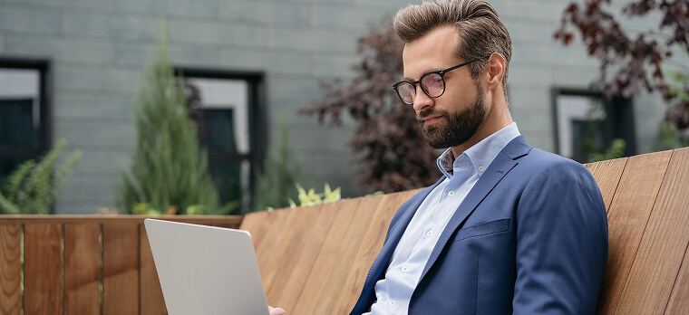 Homem com barba e óculos usando laptop em ambiente externo